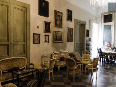 Compongono l'arredamento sedie e poltrone color verde oliva, piccoli tavoli rotondi e vetrinette vintage ornate con pezzi di ceramica